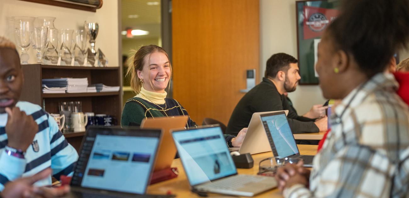 Students talk while working at their computers.