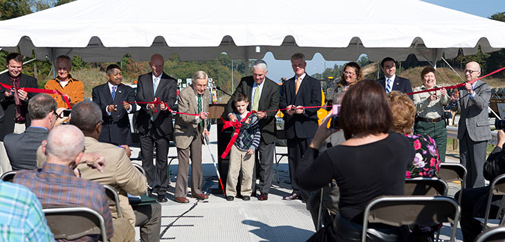 People line up to cut a red ribbon at a new road