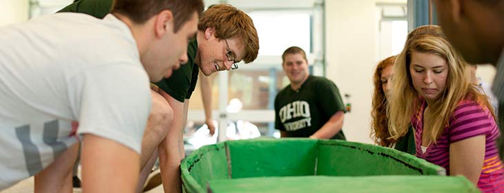 A group of students bend to lift a handcrafted-looking object