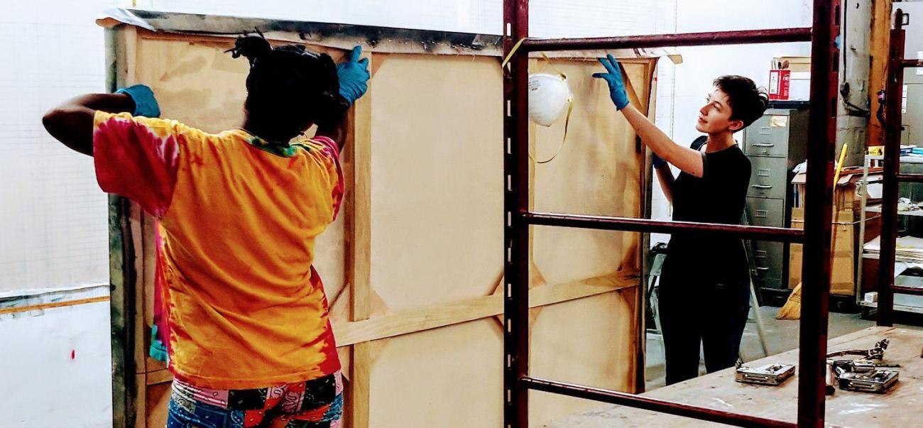 Students handle large painting with scaffolding in studio