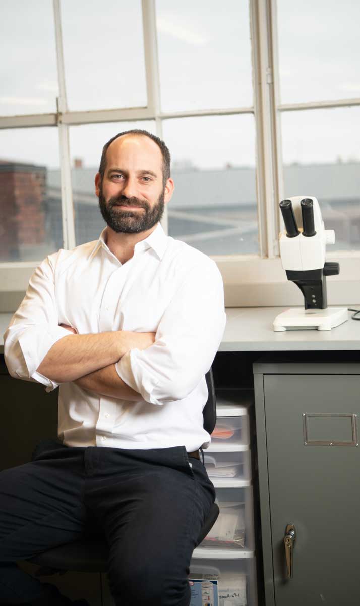 Assistant professor of anthropology, Joseph Gingerich, poses in his lab next to a microscope.
