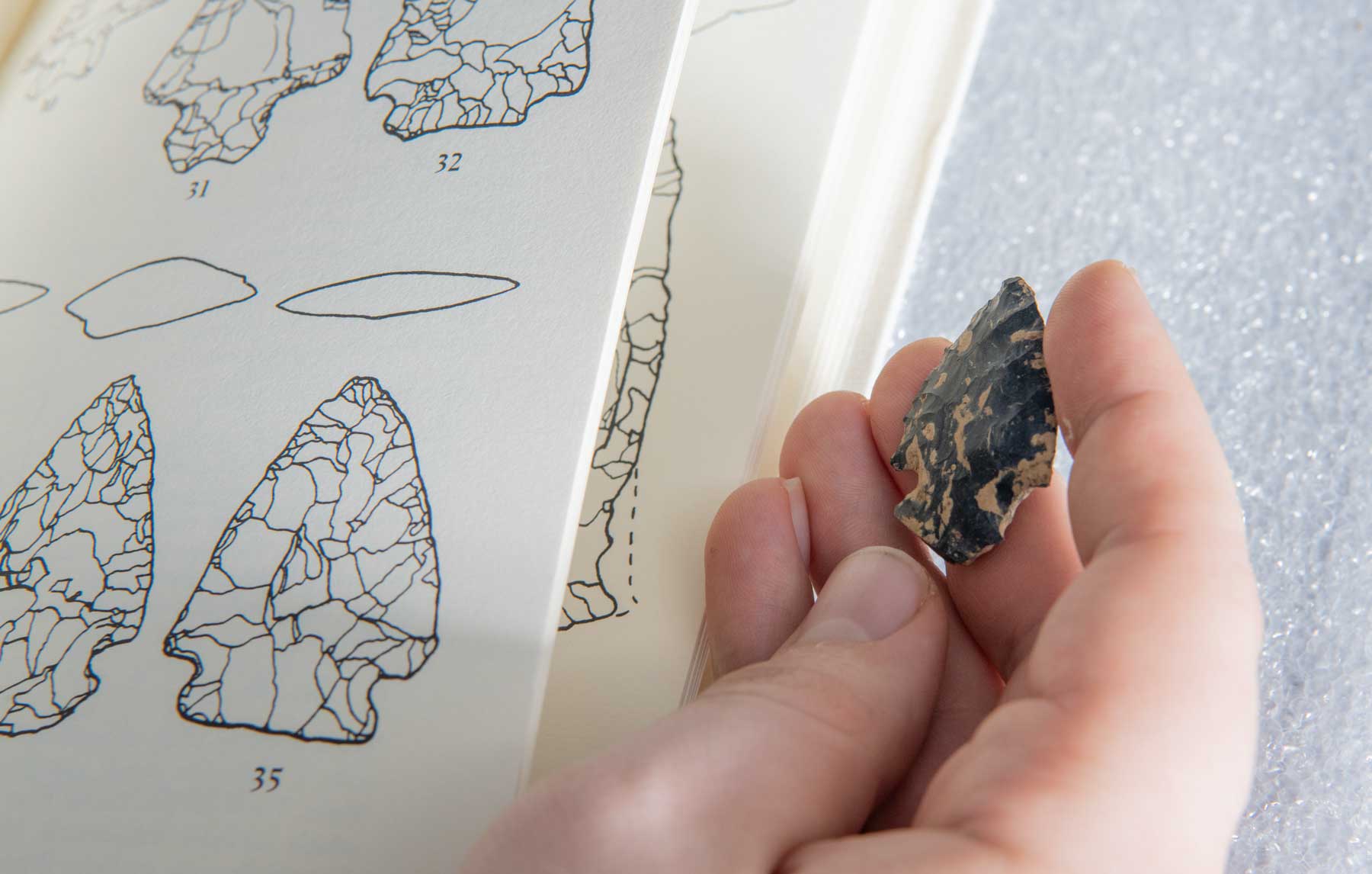 Image of an arrowhead identification book next to a stone arrowhead in a person's hand