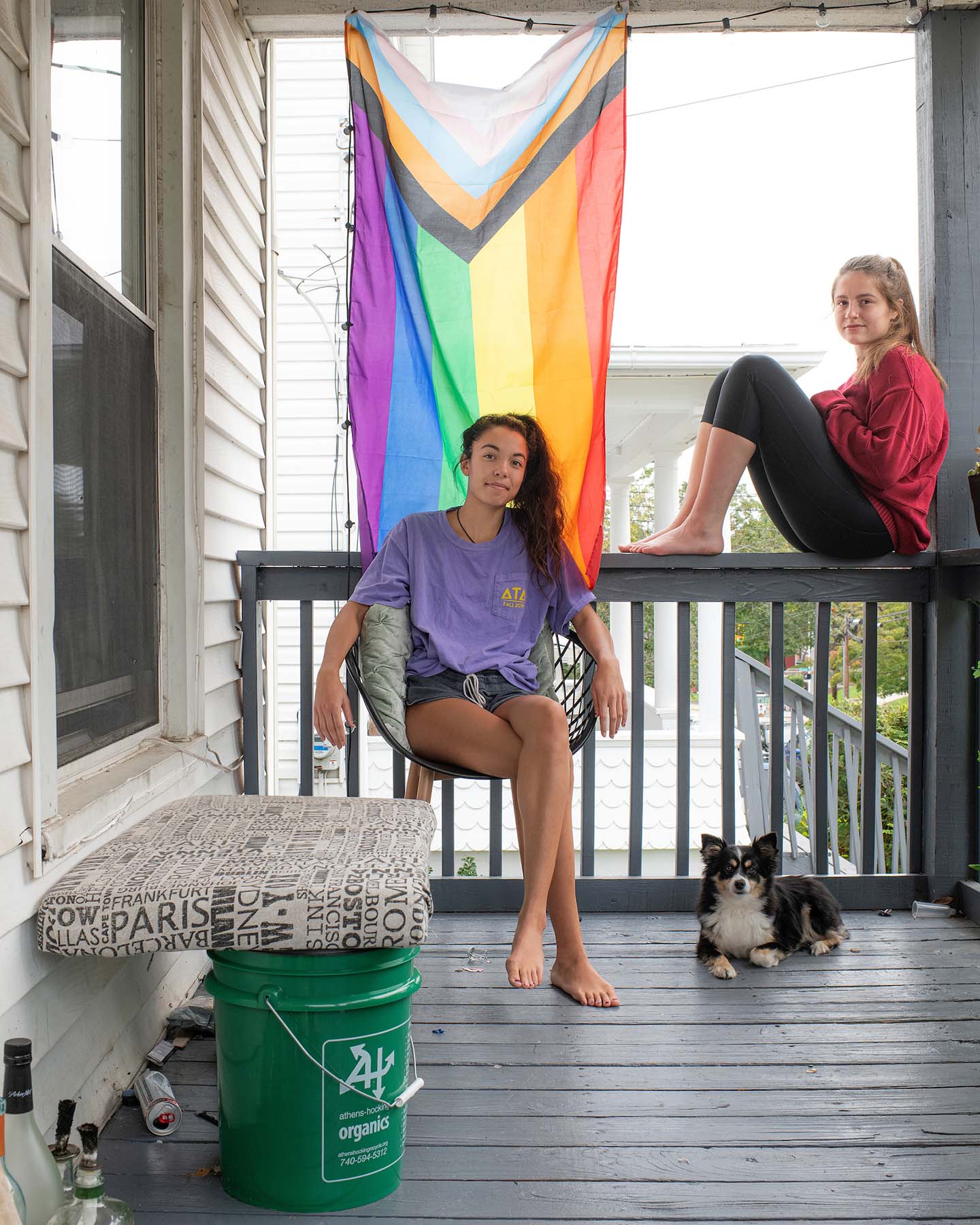 Students with their dog posing on their front porch with their pride flag