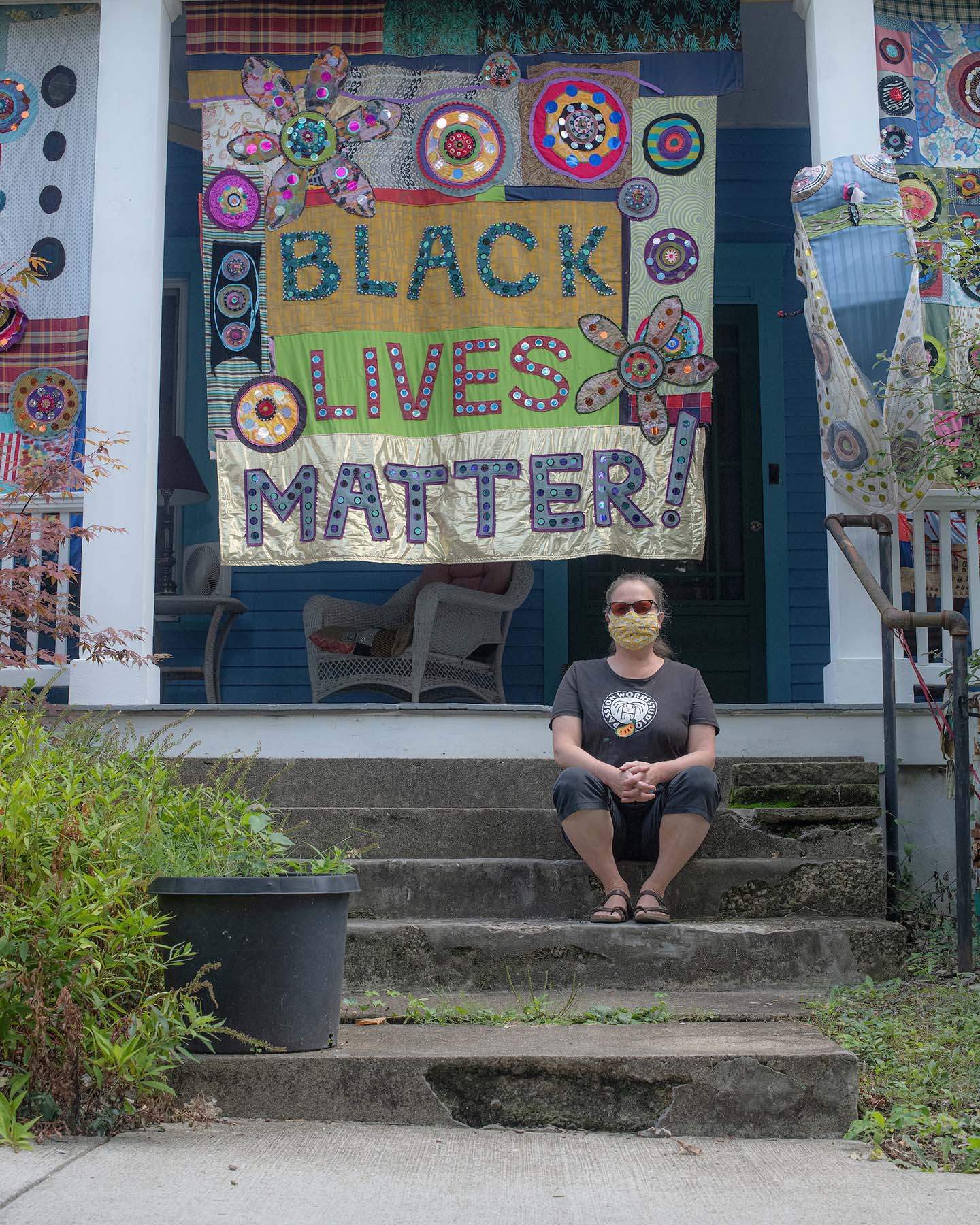 Patty Mitchell posing on her front porch with a giant, handmade social justice banner
