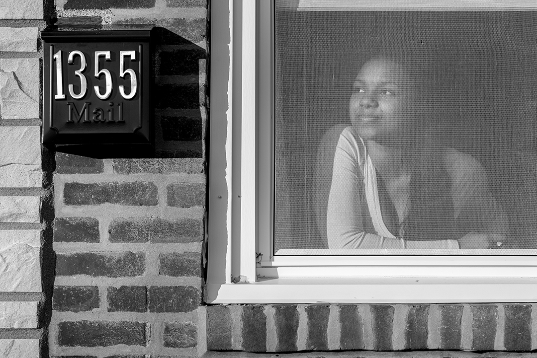 A woman looks out her screened window