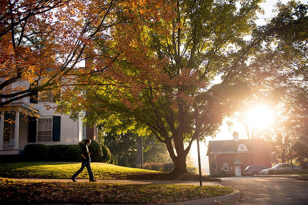 The sun rises behind fall foliage as a student walks to class
