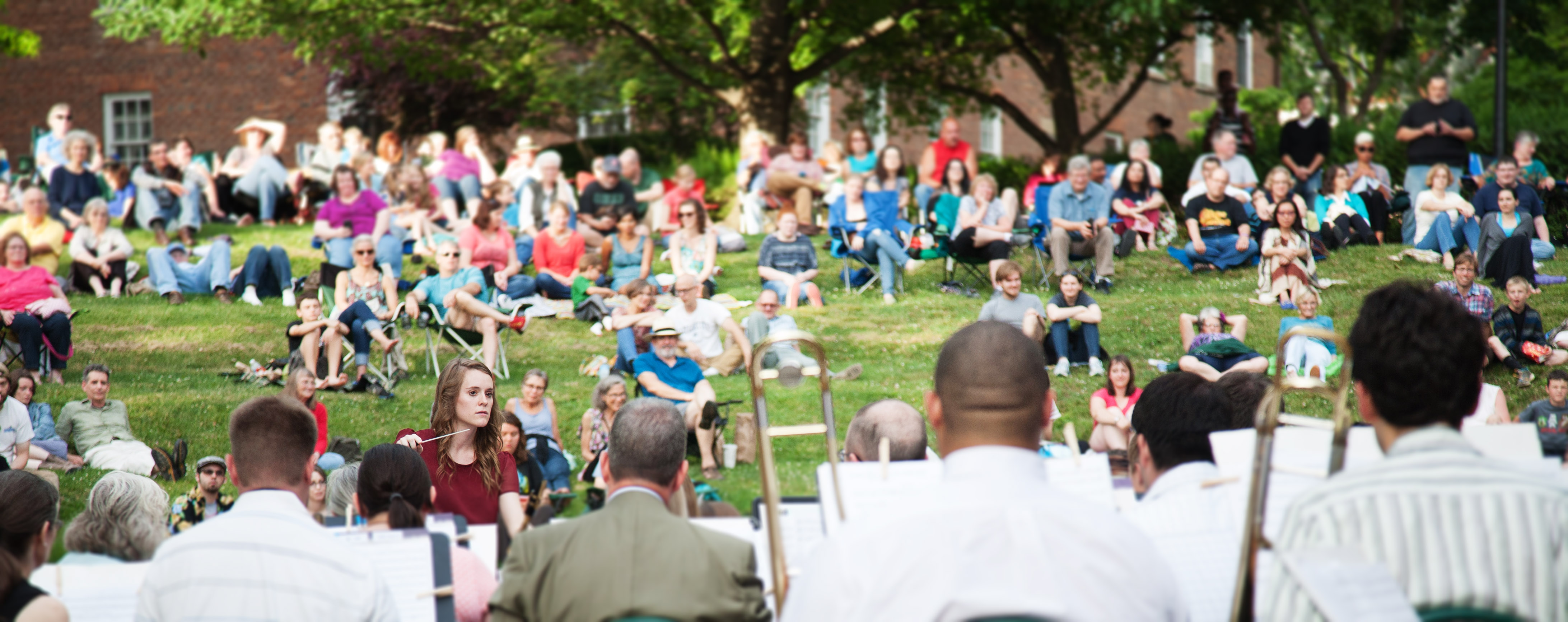 People sitting in grass looking onward and listening to a band