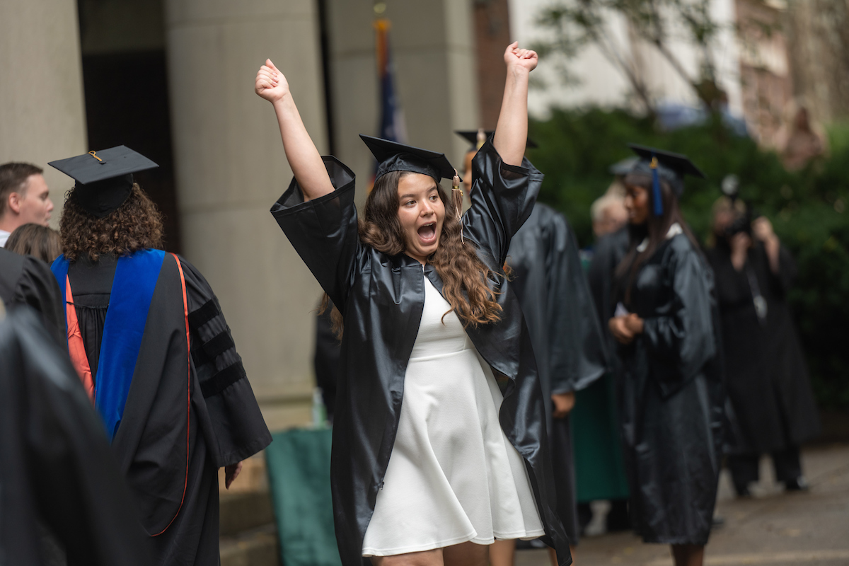 Student at commencement with their hands in the air in celebration