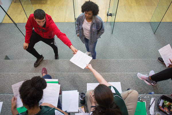 Students sit on stairs of Copeland Hall. One passes another a piece of paper