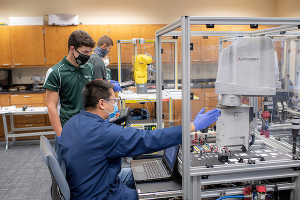 A teacher and a student sit at a 3D printer