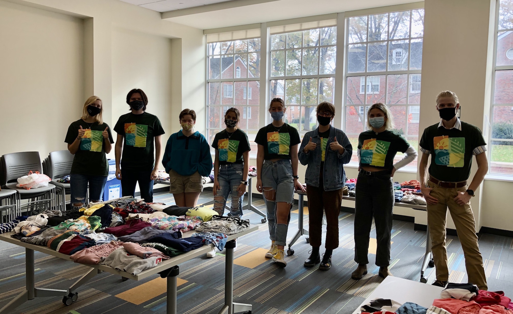 A group of ambassadors stand by tables full of shirts