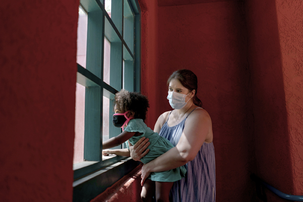 Kristina Woldan, a frontline nurse, holds her daughter Zoe up to a window at the Los Angeles Zoo
