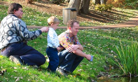 Andreas Weichselbaum, a friend, and a young child sit by the pond in Emeriti Park