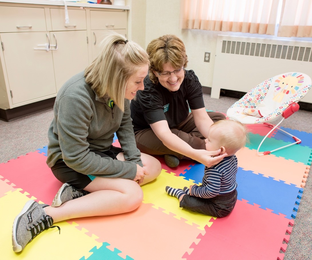 Two women on a play mat with a baby