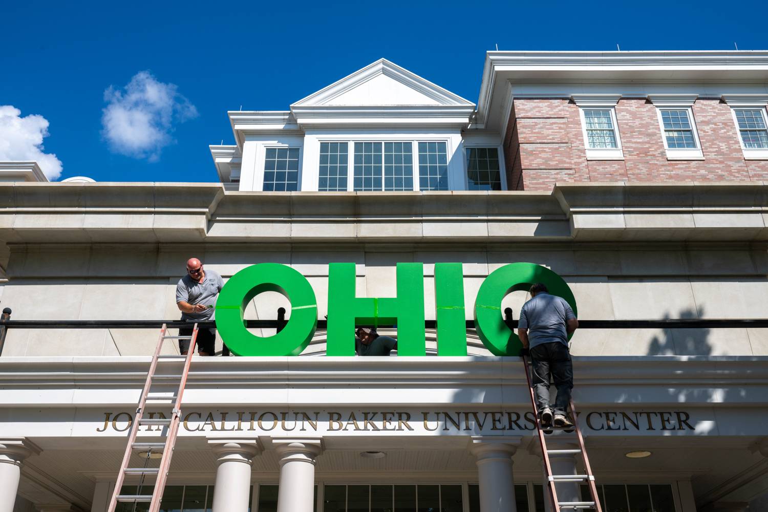 OHIO employees install a sign on Baker Center in preparation for homecoming festivities.