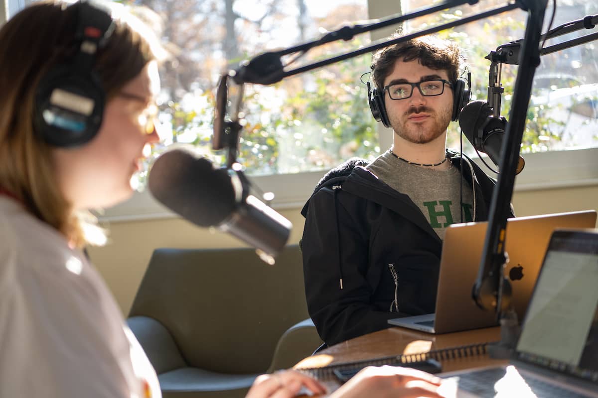 Two students in Scripps College of Communication sitting and talking at mics on a desk mic stand