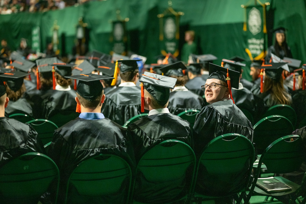 Male graduate wearing glasses looks over his shoulder at the camera during Fall 2023 Commencement ceremony