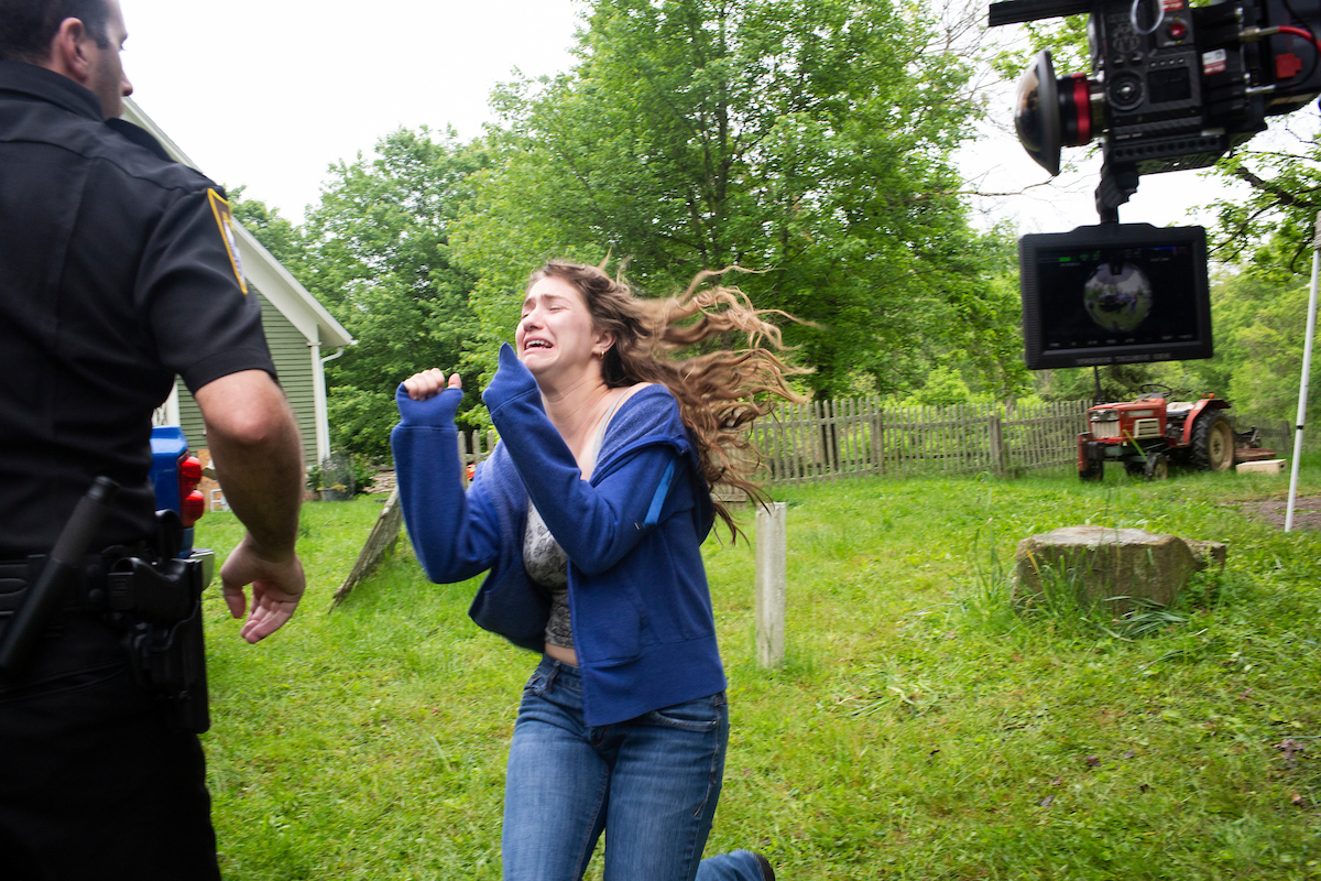 An actor portraying a woman in distress runs across a lawn.