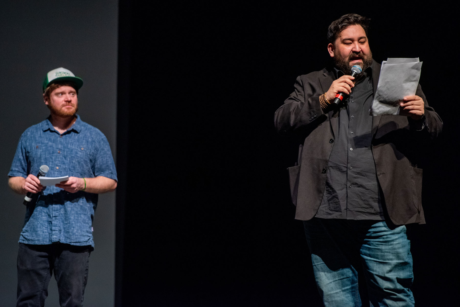 Two men on stage announce a contest winner while holding a piece of paper