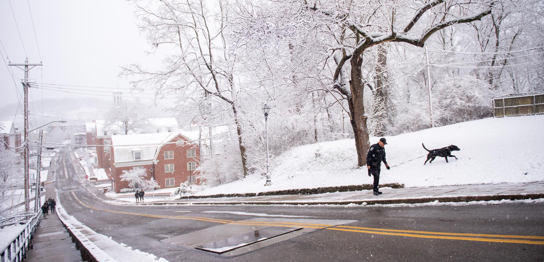 An OUPD K9 officer walks up a snowy Jeff Hill on Athens Campus