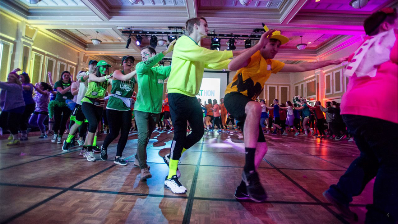 A large group of students dressed in costumes forming a circle train and dancing