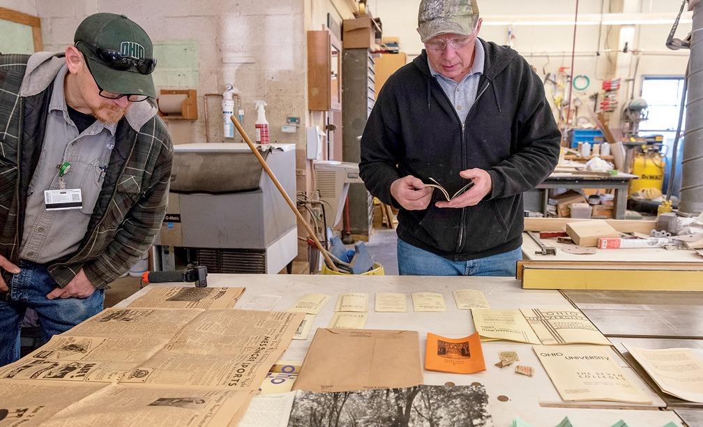 Two men look over papers and booklets on a table.