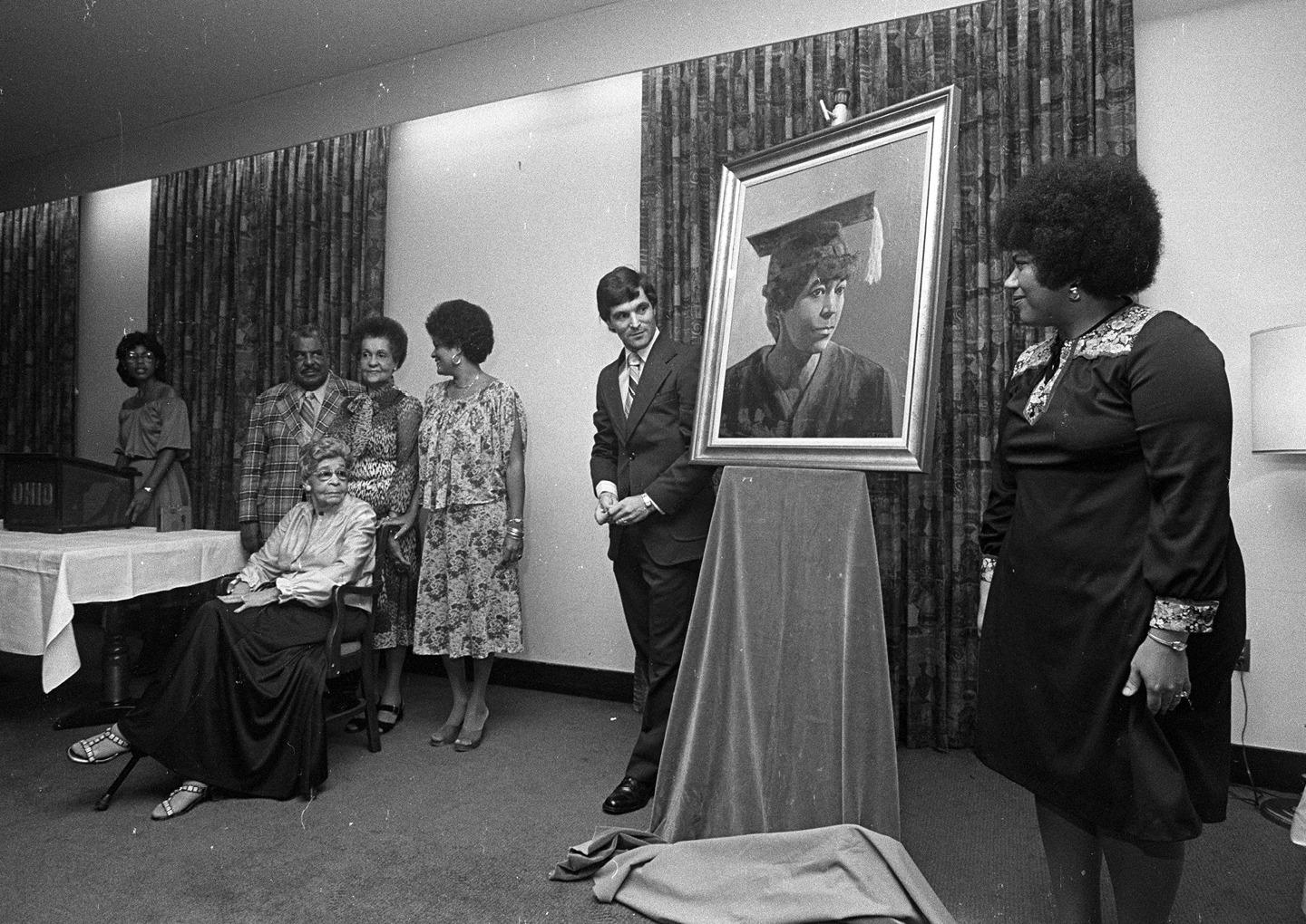 Martha Jane Hunley Blackburn [SEATED] is seen with her 1916 yearbook graduation painting at a 1979 reception held in her honor. In 1999, Alumni Memorial Auditorium was renamed in honor of Blackburn, OHIO’s first Black female graduate, and John Newton Templeton, the University’s first Black male graduate, who earned his Ohio University degree in 1828. The East Portico of the building houses the African American Alumni Heritage Wall. Photo courtesy of the Mahn Center for Archives and Special Collections