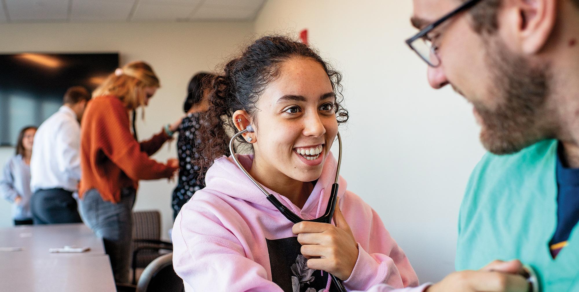 A woman places a stethoscope on a man's chest while she smiling.