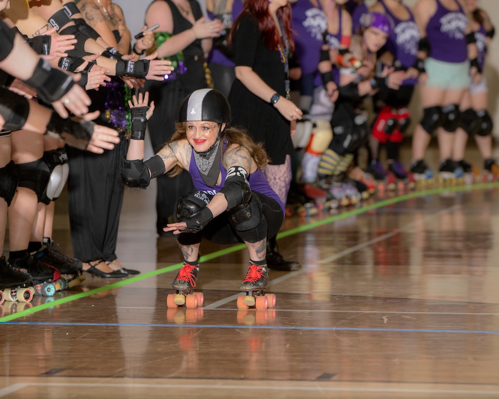 A roller derby athlete skates by a line-up of teammates giving high-fives