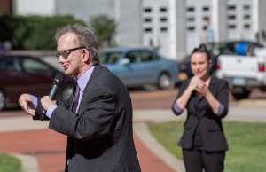 A man wearing a suit stands outside giving a speech into a microphone