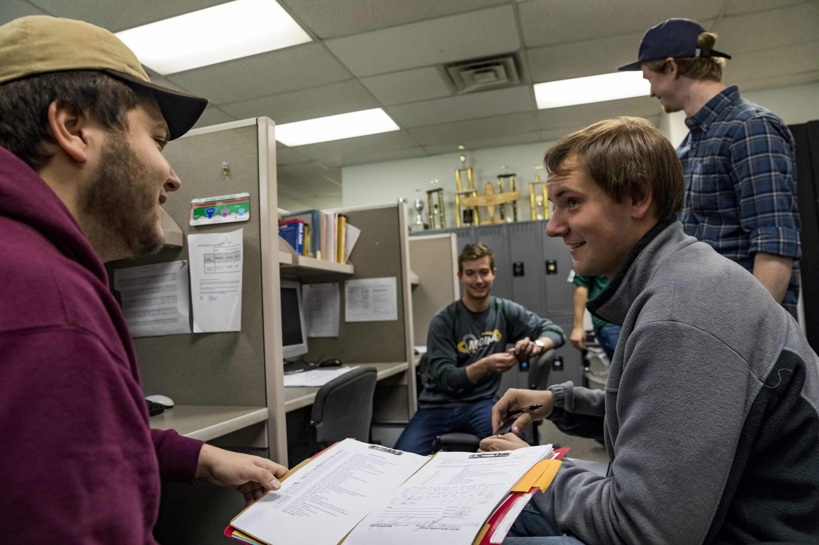 Four students sitting and talking with papers in hand