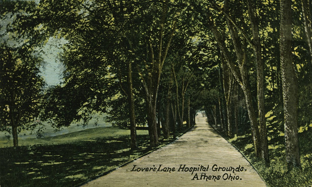 Post card of a road surrounded by trees. bottom corner says "Lover's Lane Hospital Grounds, Athens, Ohio."