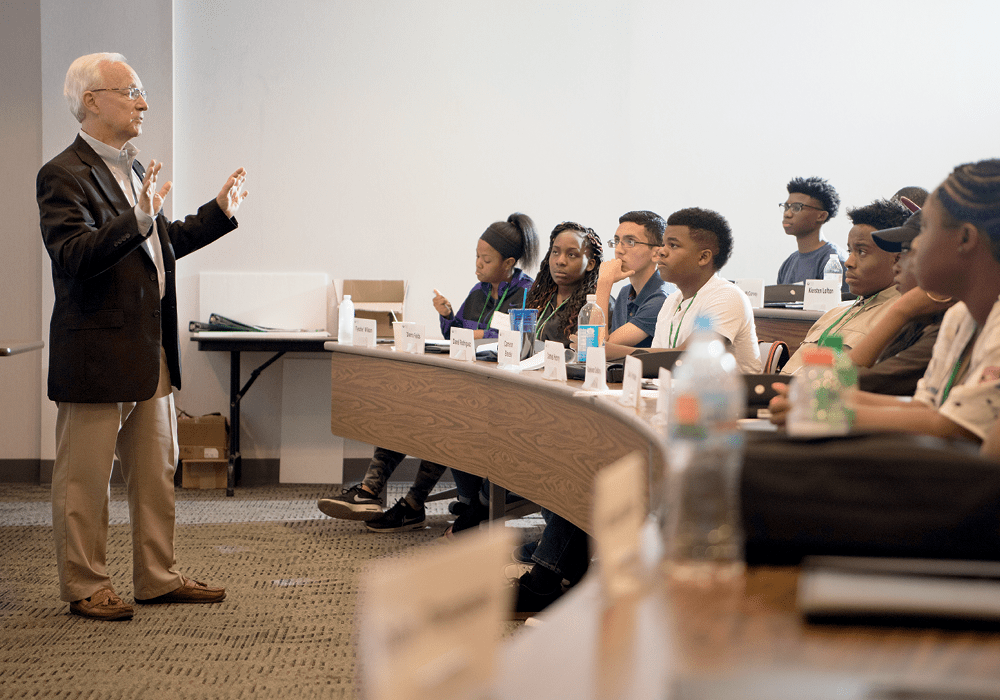 President Sherman speaking to a class room of students. He is standing in the front of the lecture room