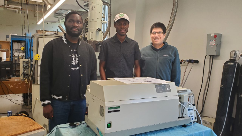 Three students pose for a picture standing behind a machine called a CD spectrometer