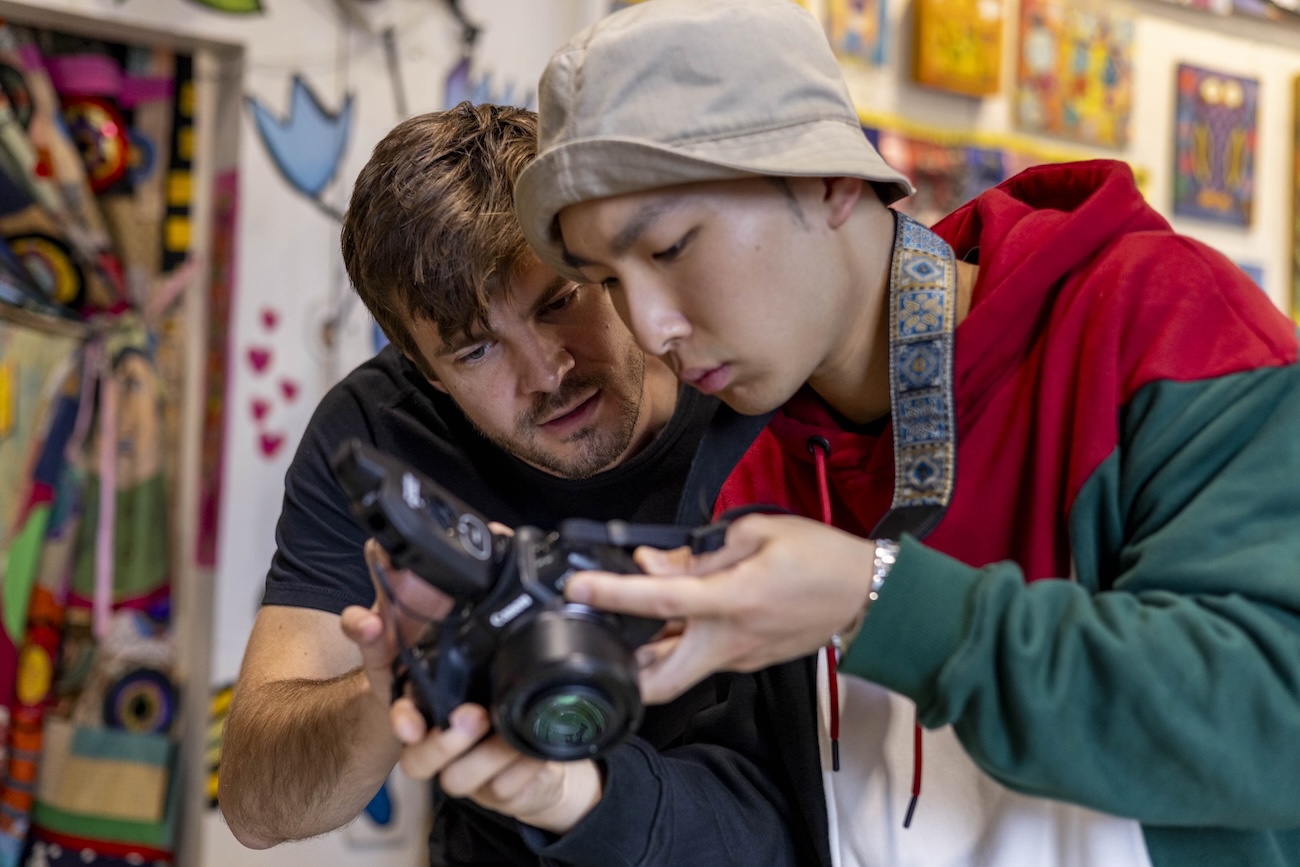 Two men look closely at the screen of a camera one of them is holding