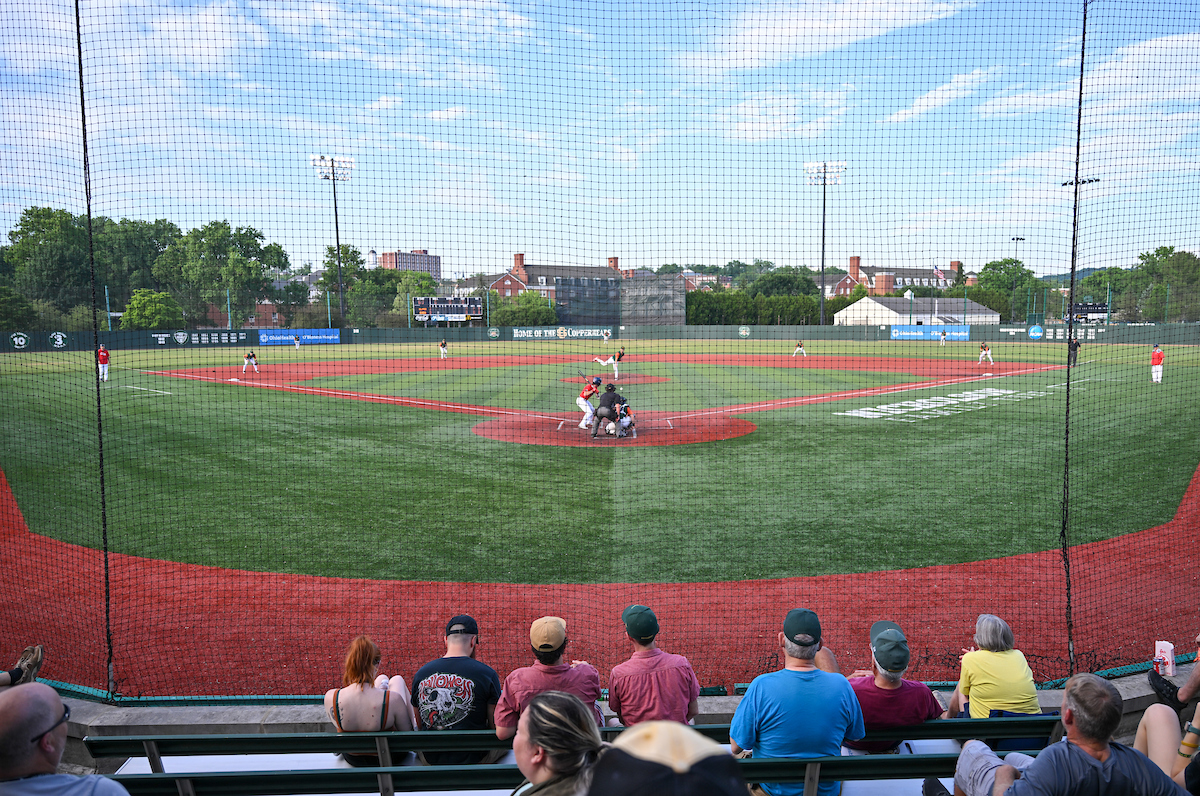 Wide shot of a baseball diamond taken from the bleachers behind home base, with spectators watching the game in the foreground