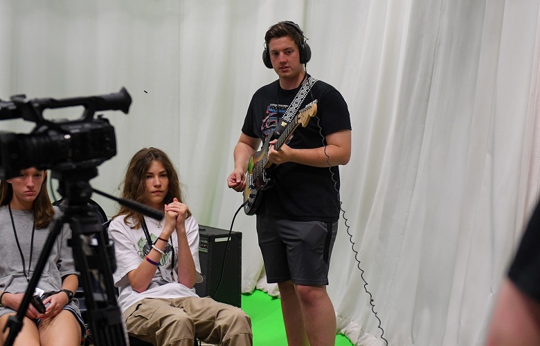 A student plays guitar while others look on at the High School Media Workshop