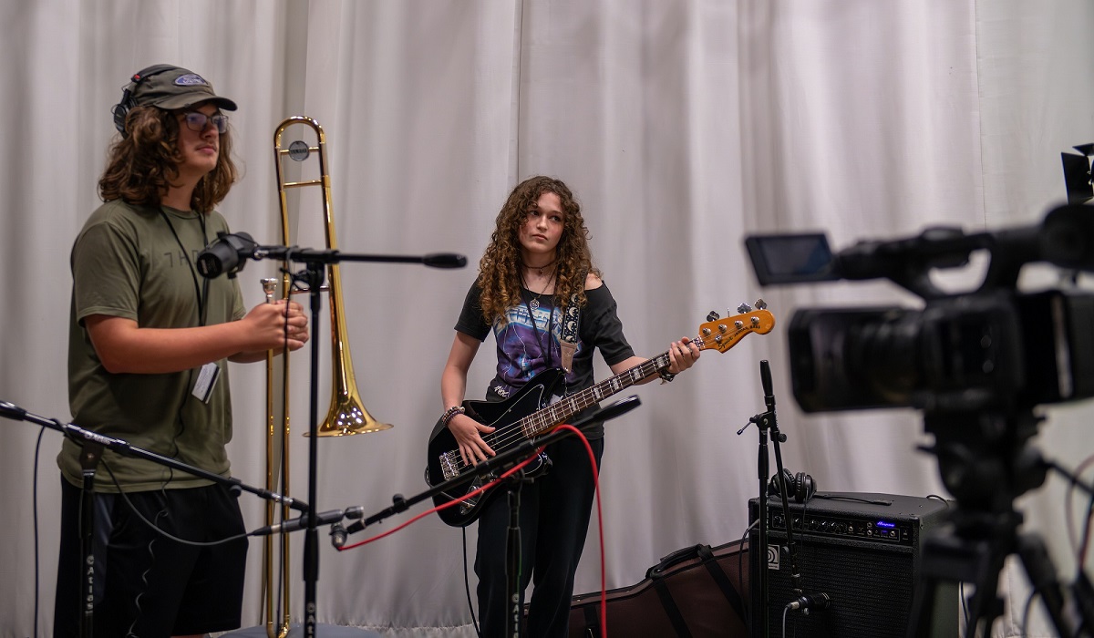 Students play musical instruments in front of media equipment at the High School Media Workshop