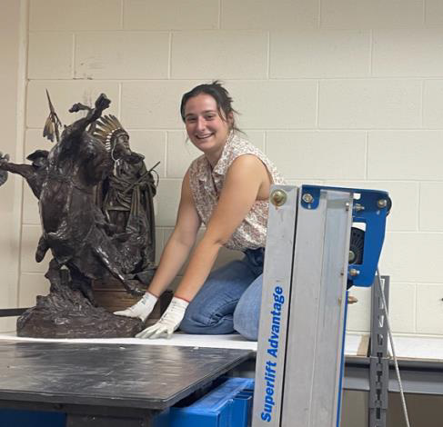 Jacquelyn Stout kneels on a table as she prepares to relocate a bronze sculpture.