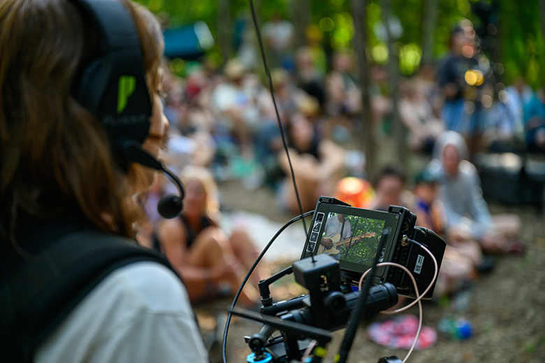 An OHIO student films a performance on the Creekside Stage using a camera with a weighted gimbal to stabilize the footage.