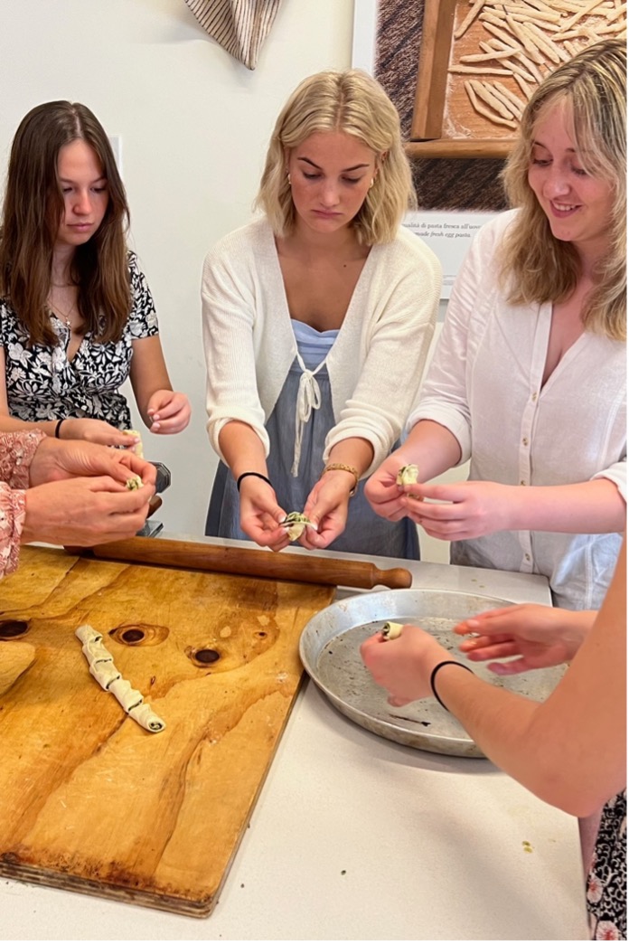 a group of women assemble small pockets of pastry