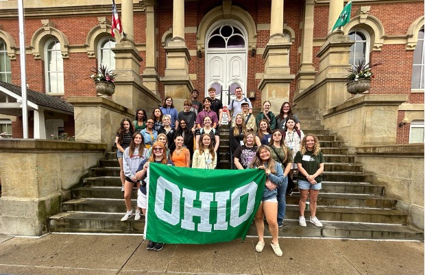 A group of students pose on stone steps with an OHIO flag