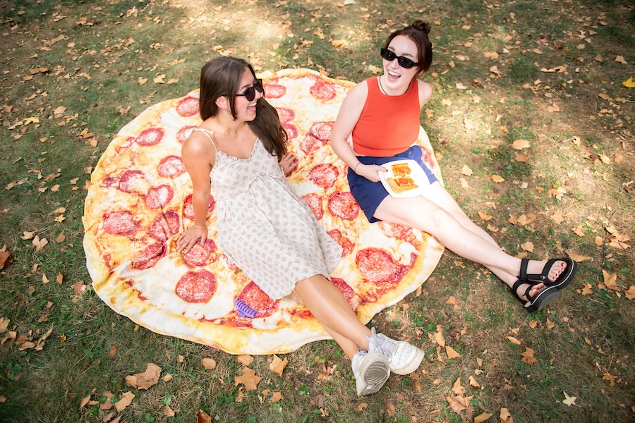 Two students sit on a blanket designed to look like a slice of pepperoni pizza