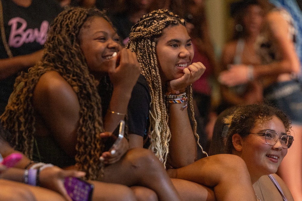 Two students watch a performance, laughing