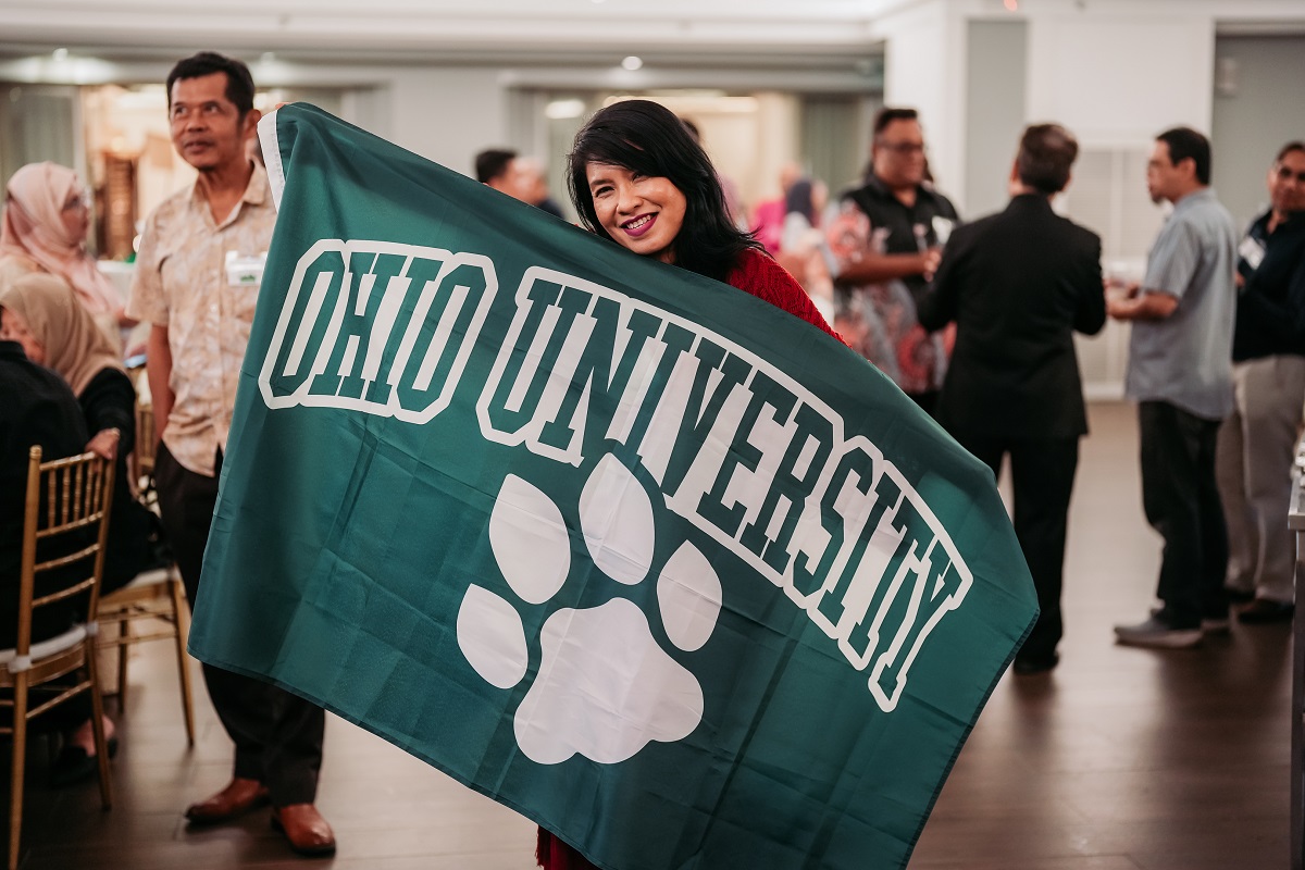 An OHIO graduate holds up an Ohio University flag during an alumni event in Malaysia