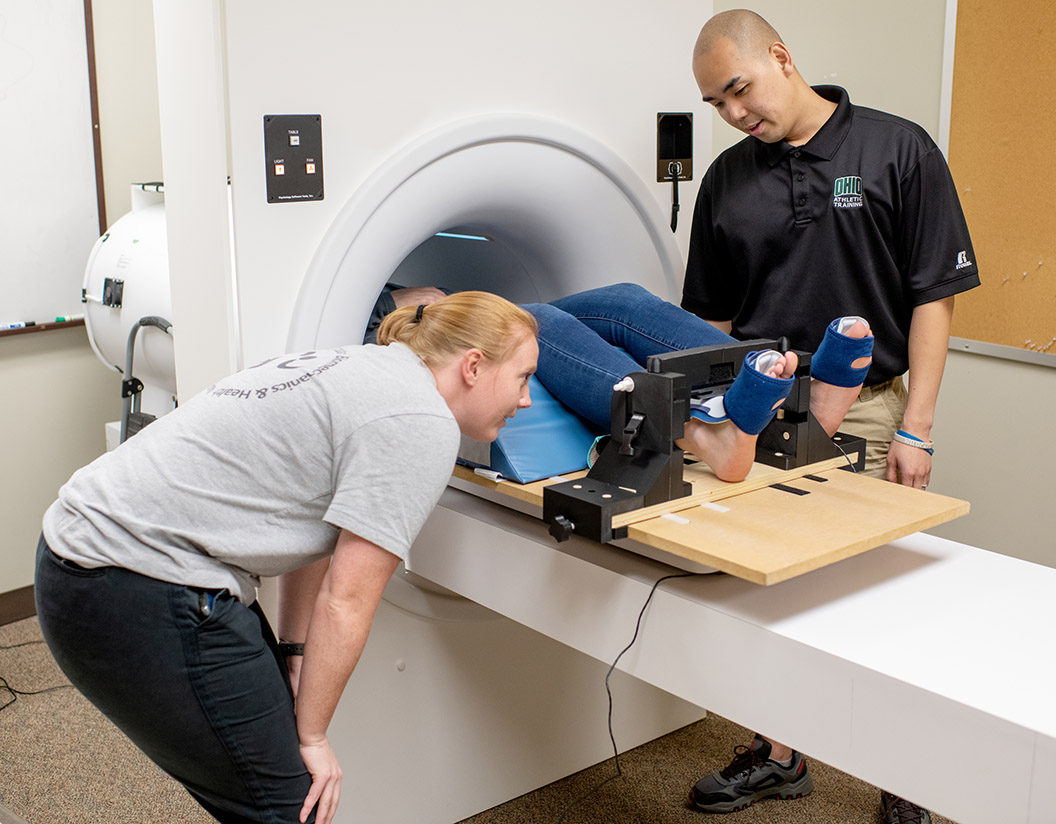 researchers in street clothes place a patient on an MRI machine