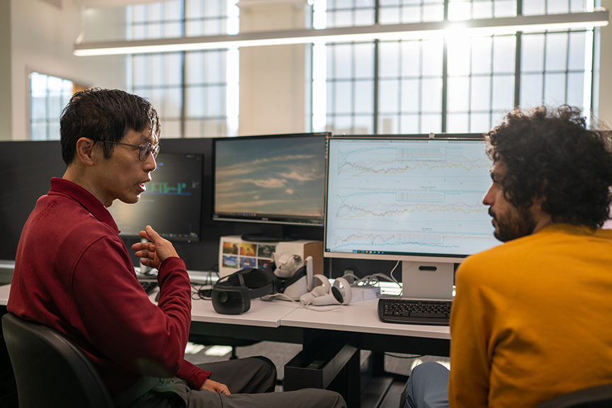 two researches collaborate while sitting in front of a computer and window 