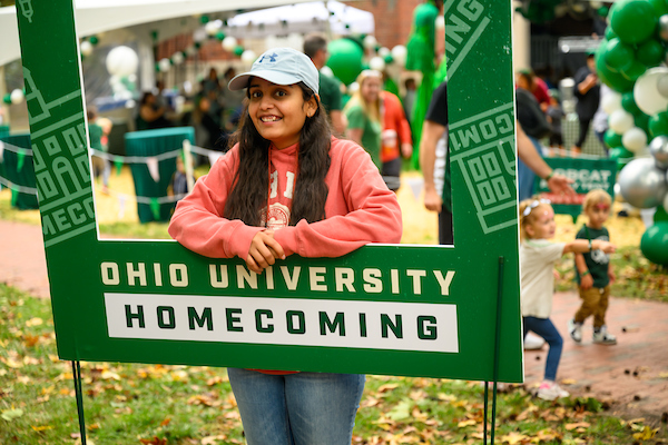 An individual poses in a large framed Homecoming sign.