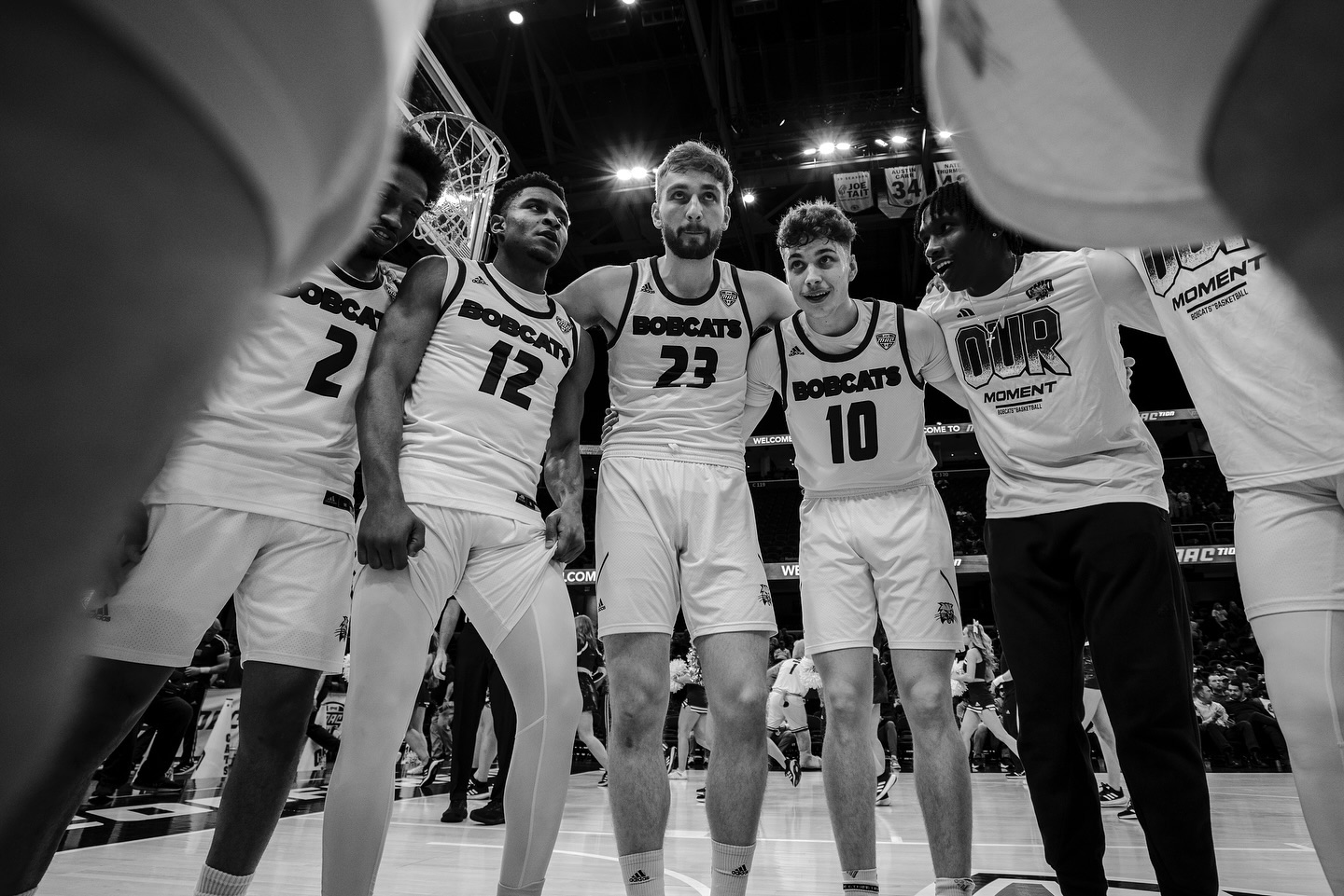 a black and white photo of Ohio University men's basketball players in a huddle