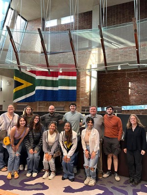 Group of people pose inside building under a flag